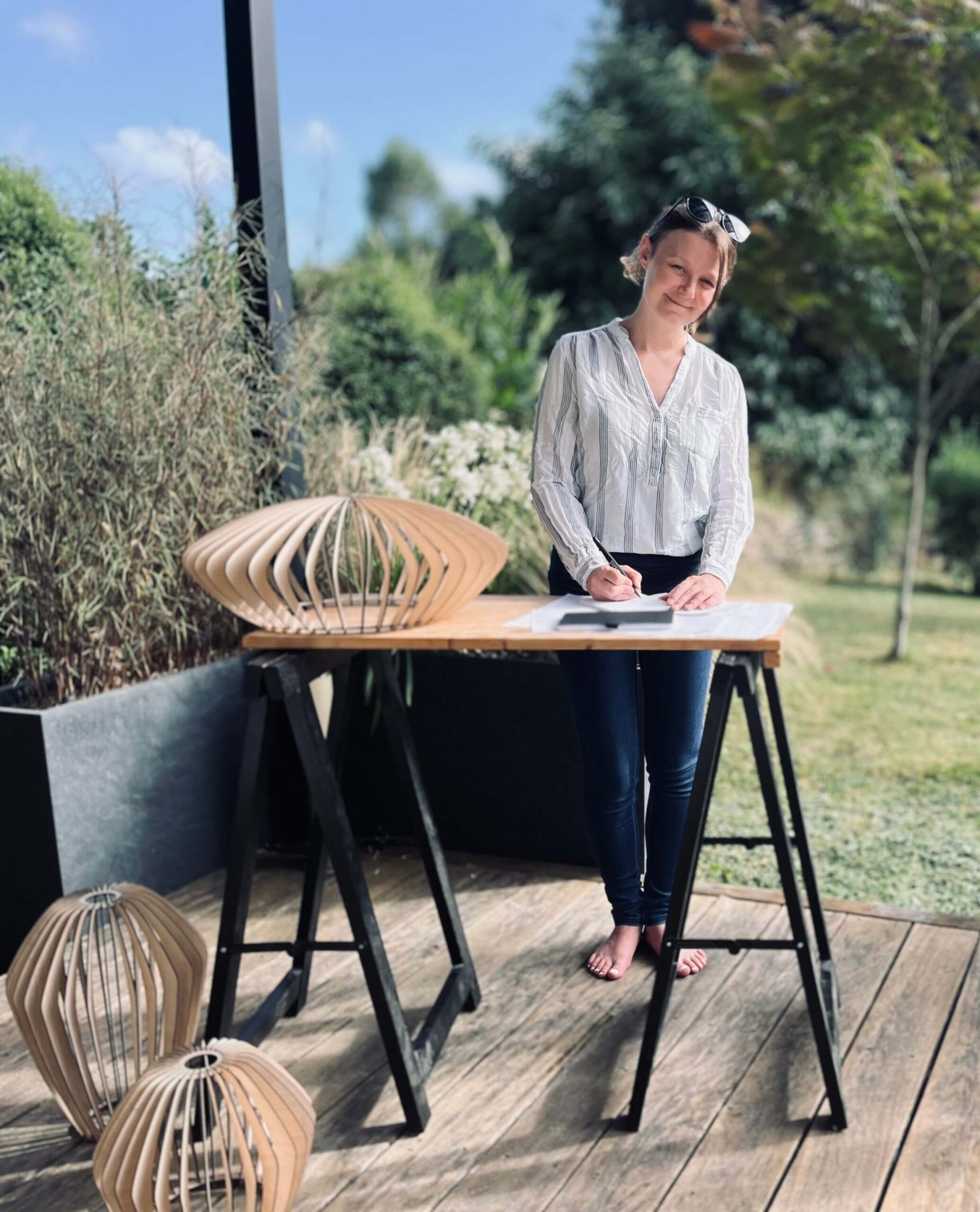 Photo d'une personne dehors sur une terrasse en train de dessiner avec des luminaires en bois posés sur le sol et la table